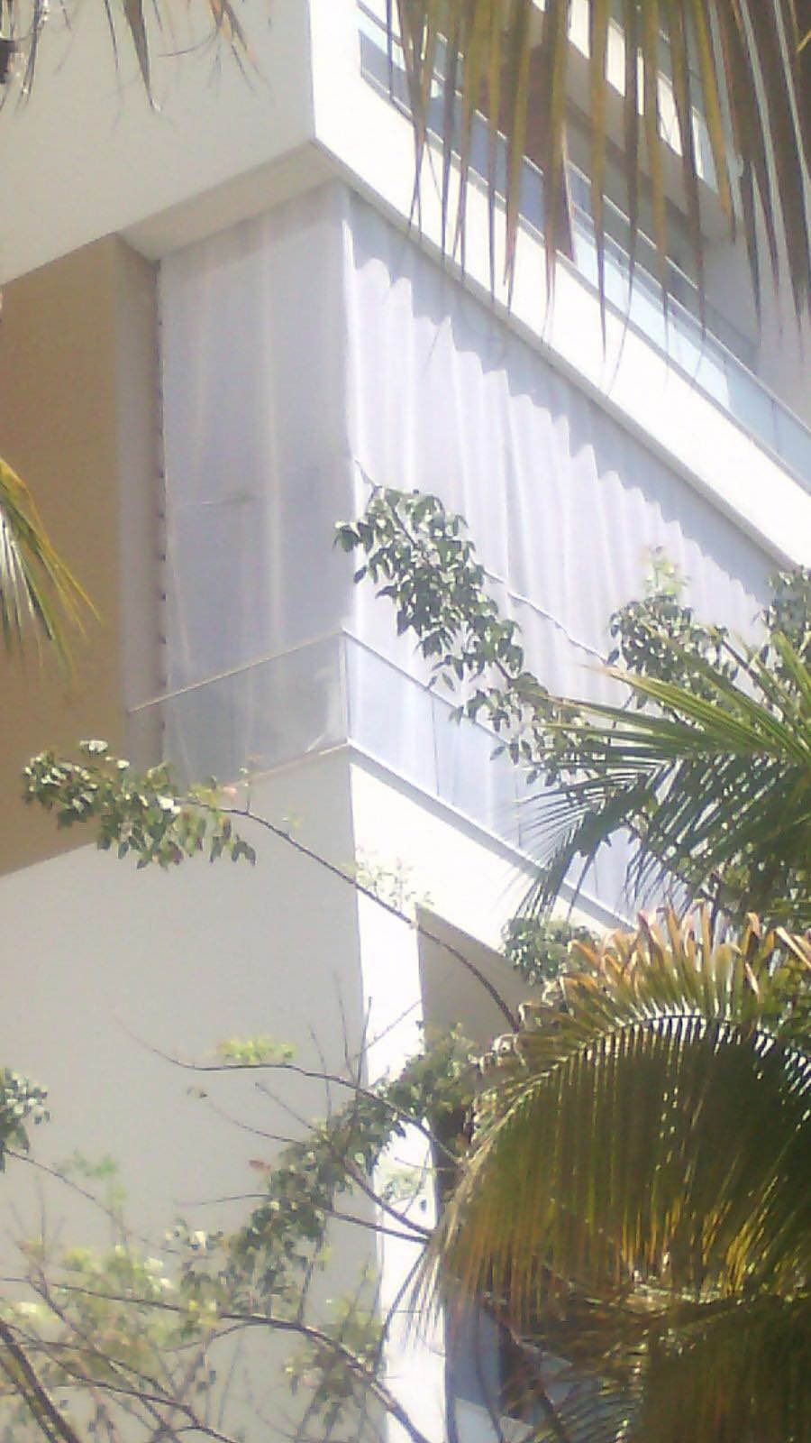 Tall AquaGrid screen beside facade columns, viewed from a garden with palm trees.